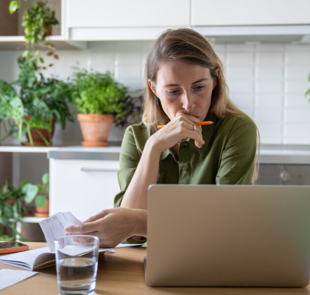 Pensive sorrowful woman reviewing bills with laptop and glass of water in home kitchen. Financial stress, debt issues, utility pay, household budget finance struggles, overdue accounts, money problems
