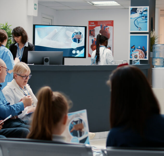 Busy hospital reception with diverse group of patients in waiting room area, having consultation appointment with specialist for healthcare treatment. Reception desk in facility lobby.
