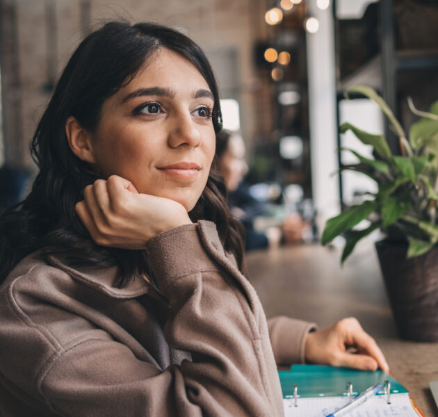 Attractive smiling young woman makes notes in her notebook in a cafe.Remote work,business,freelance concept.